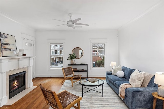 living room featuring a ceiling fan, visible vents, a fireplace with flush hearth, ornamental molding, and light wood-type flooring