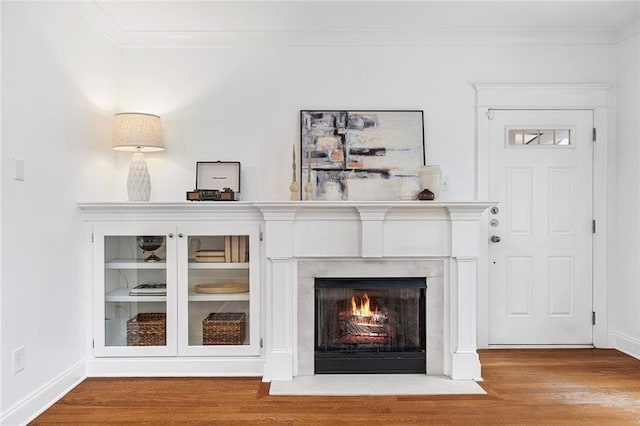 interior details featuring a fireplace with flush hearth, crown molding, baseboards, and wood finished floors