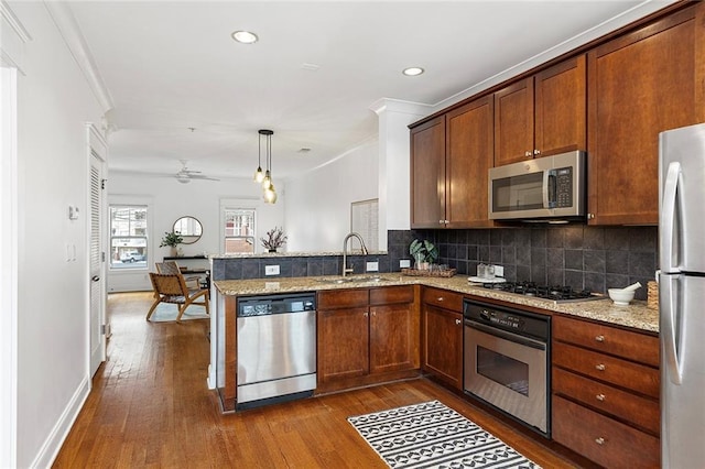 kitchen with a sink, dark wood-style floors, appliances with stainless steel finishes, a peninsula, and decorative backsplash