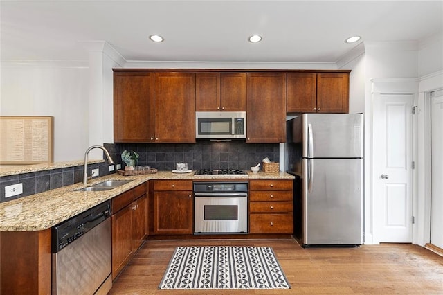 kitchen with light stone counters, a sink, stainless steel appliances, light wood-style floors, and tasteful backsplash