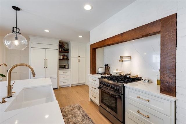 kitchen with light wood-style flooring, a sink, white cabinets, high end stainless steel range oven, and pendant lighting