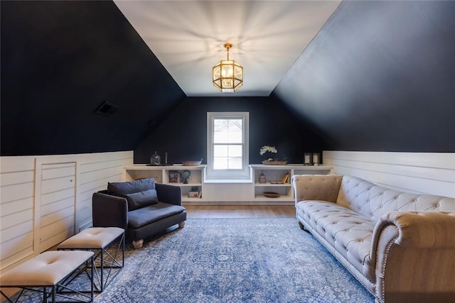 living area with lofted ceiling, wooden walls, an inviting chandelier, and wood finished floors