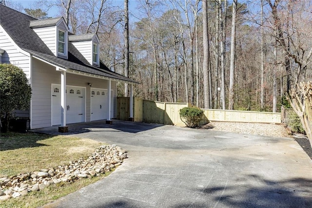 view of home's exterior with a garage, fence, driveway, and a shingled roof