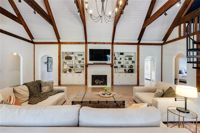 living area with vaulted ceiling with beams, a fireplace with flush hearth, arched walkways, and wood finished floors