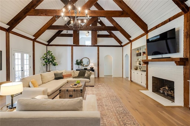 living area featuring built in features, arched walkways, beam ceiling, light wood finished floors, and a brick fireplace