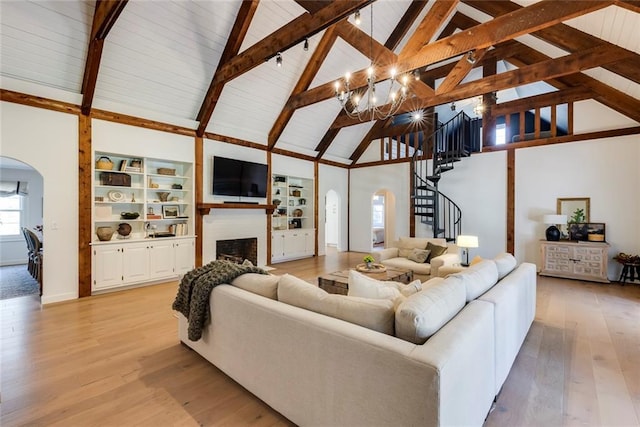 living area with arched walkways, a fireplace, stairway, light wood-style floors, and beamed ceiling