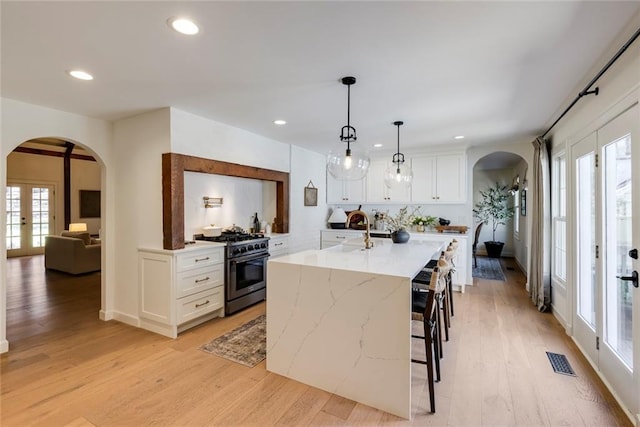 kitchen with arched walkways, french doors, stainless steel range, visible vents, and light wood-style floors