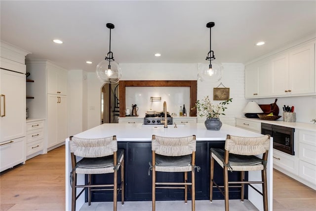 kitchen featuring arched walkways, white cabinets, built in microwave, light countertops, and a sink