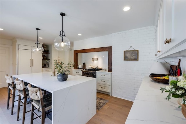 kitchen with light wood finished floors, a kitchen bar, range with gas cooktop, and white cabinetry