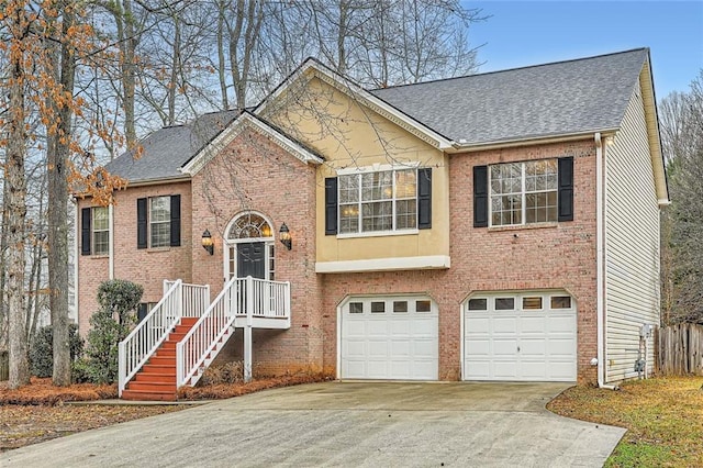 split foyer home with a garage, concrete driveway, brick siding, and roof with shingles