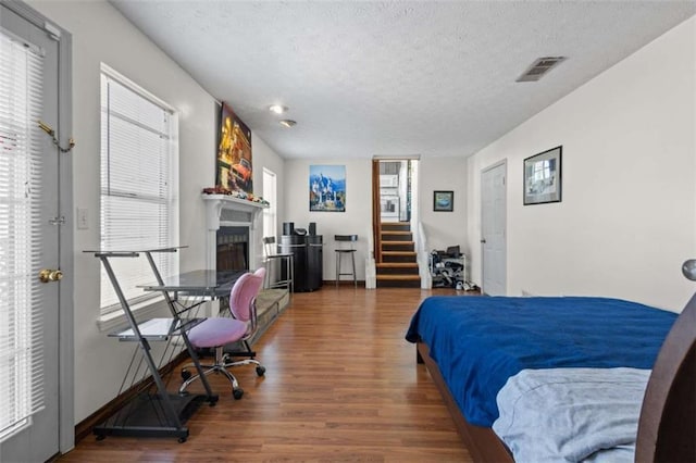 bedroom featuring wood finished floors, a textured ceiling, a fireplace, and multiple windows