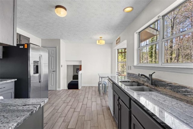 kitchen featuring stainless steel fridge, a sink, light wood-style floors, baseboards, and light stone countertops