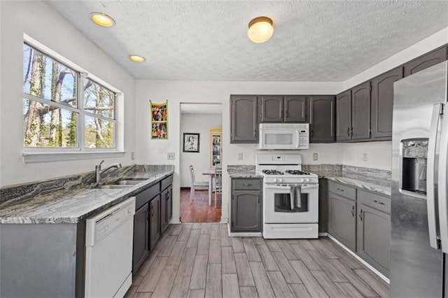 kitchen featuring white appliances, light wood-type flooring, a sink, a textured ceiling, and recessed lighting