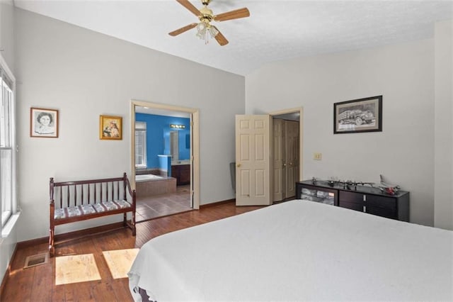 bedroom featuring wood finished floors, vaulted ceiling, baseboards, ensuite bath, and ceiling fan