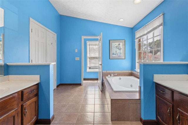 full bathroom with vanity, baseboards, a jetted tub, vaulted ceiling, and tile patterned floors