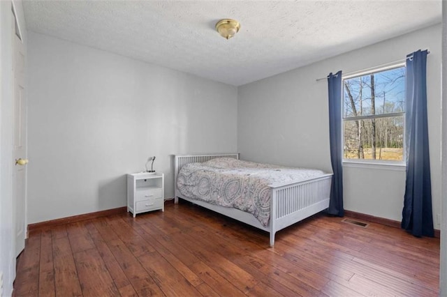 bedroom with wood-type flooring, baseboards, and a textured ceiling