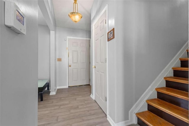 hall featuring light wood-type flooring, stairs, and baseboards