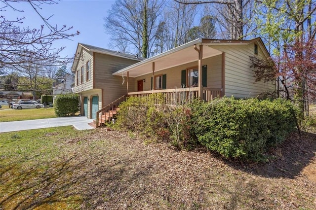 view of front facade with covered porch, concrete driveway, a garage, stairway, and a front yard