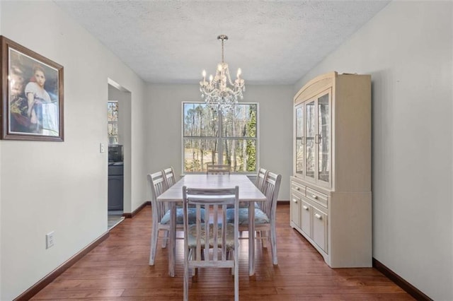 dining space featuring a chandelier, wood finished floors, a textured ceiling, and baseboards