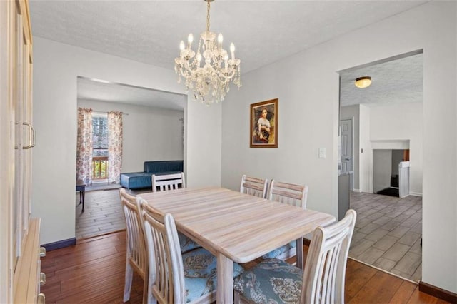 dining space featuring wood finished floors, a chandelier, a textured ceiling, and baseboards