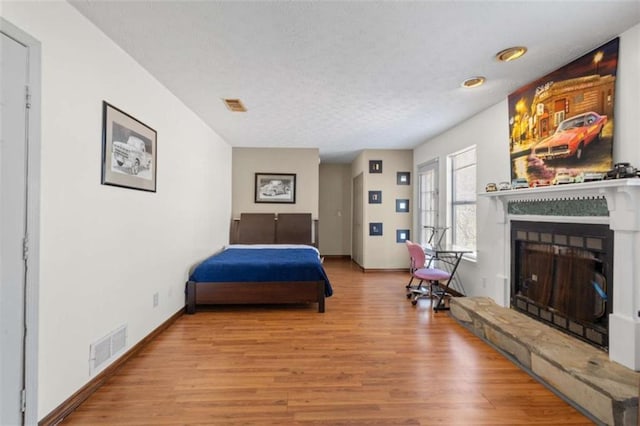 bedroom featuring wood finished floors, a fireplace with raised hearth, a textured ceiling, and baseboards