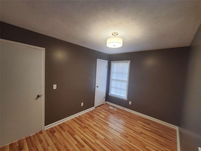 spare room with light wood-type flooring and a textured ceiling