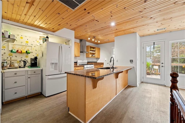 kitchen featuring wall chimney range hood, white appliances, sink, dark stone counters, and light wood-type flooring