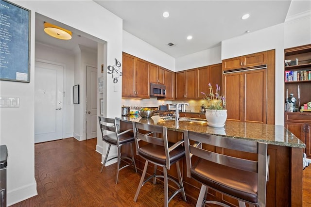 kitchen featuring tasteful backsplash, an island with sink, dark hardwood / wood-style flooring, sink, and dark stone countertops