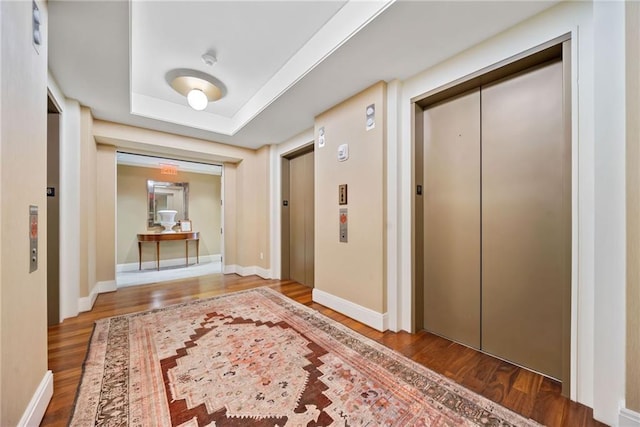 corridor with a tray ceiling, elevator, and hardwood / wood-style floors