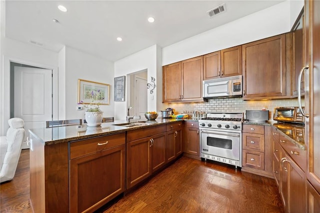 kitchen with appliances with stainless steel finishes, dark stone counters, decorative backsplash, sink, and kitchen peninsula