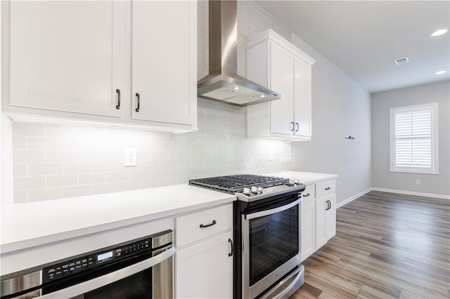 kitchen with light wood-type flooring, stainless steel gas range, white cabinetry, wine cooler, and wall chimney range hood