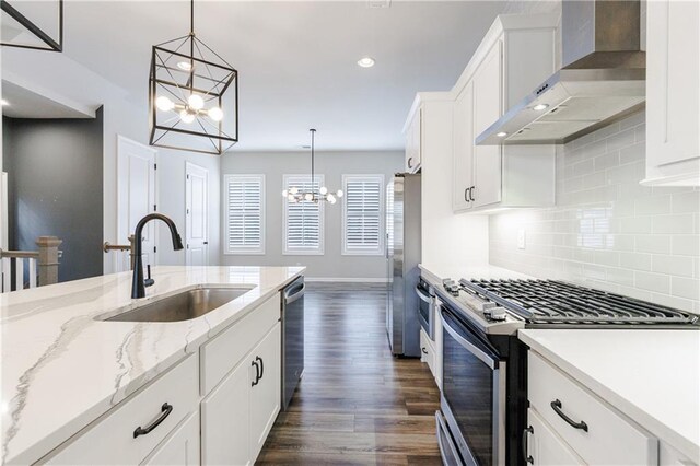 kitchen with decorative light fixtures, a notable chandelier, stainless steel appliances, wall chimney range hood, and white cabinets