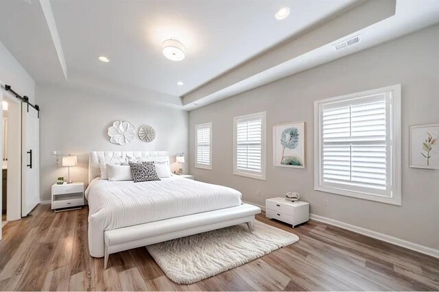 bedroom featuring light wood-type flooring, a tray ceiling, and a barn door