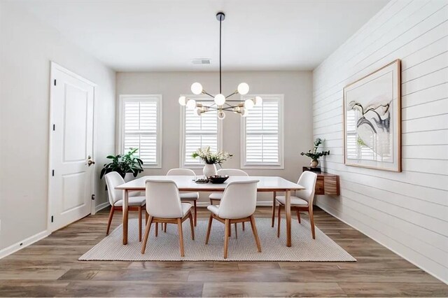 dining area featuring dark wood-type flooring, wood walls, and a notable chandelier