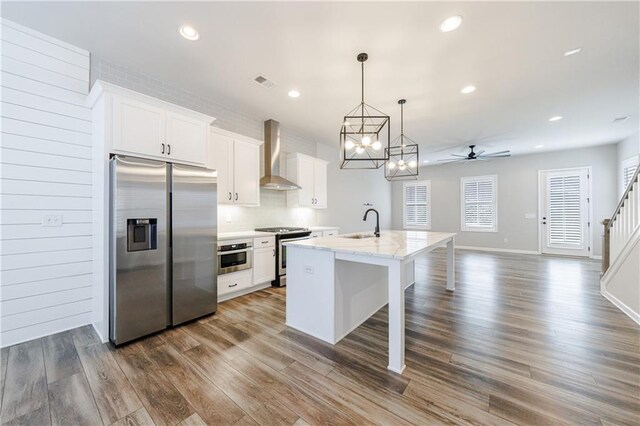 kitchen with stainless steel appliances, an island with sink, dark wood-type flooring, wall chimney exhaust hood, and white cabinets