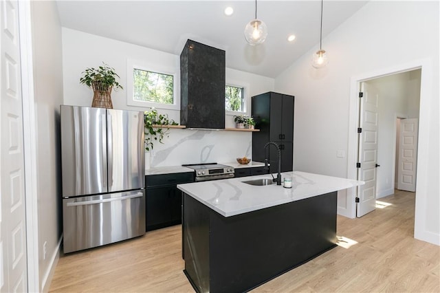 kitchen featuring a kitchen island with sink, appliances with stainless steel finishes, hanging light fixtures, light wood-type flooring, and sink