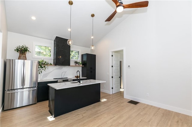 kitchen featuring decorative light fixtures, ceiling fan, light hardwood / wood-style flooring, an island with sink, and stainless steel fridge