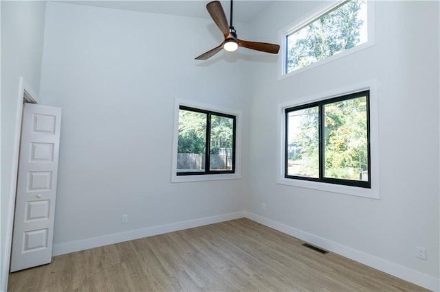 empty room featuring a towering ceiling, ceiling fan, and light hardwood / wood-style floors