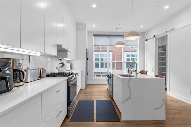 kitchen featuring white cabinets, stainless steel appliances, sink, hanging light fixtures, and a barn door