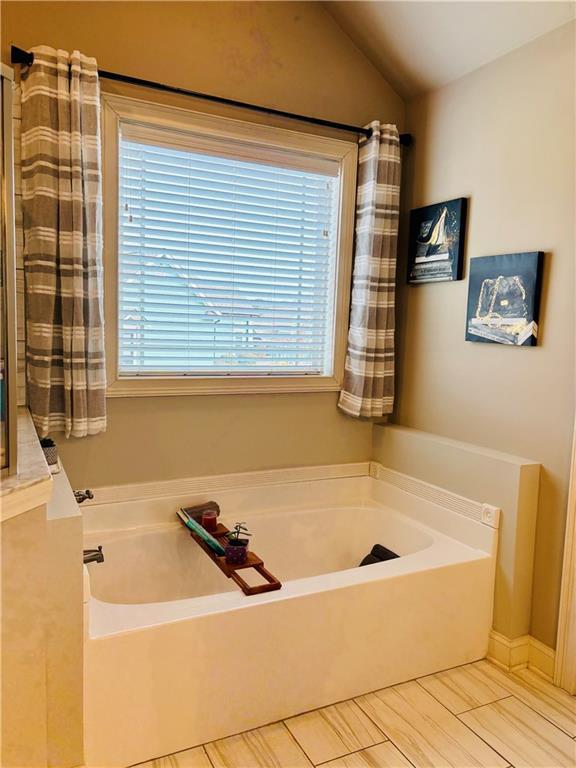 bathroom featuring a tub to relax in and vaulted ceiling