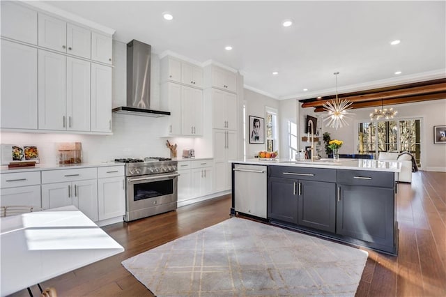 kitchen featuring pendant lighting, white cabinets, wall chimney exhaust hood, stainless steel appliances, and a kitchen island with sink