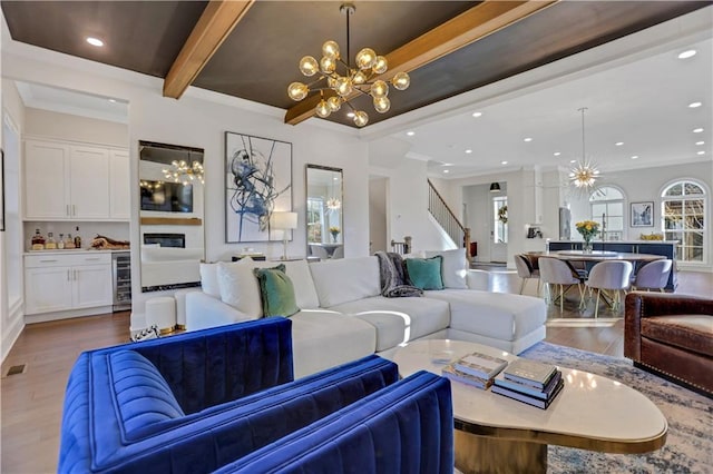 living room featuring an inviting chandelier, light hardwood / wood-style floors, wine cooler, crown molding, and beamed ceiling