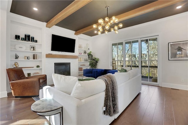 living room with built in shelves, beamed ceiling, dark hardwood / wood-style floors, a notable chandelier, and a brick fireplace