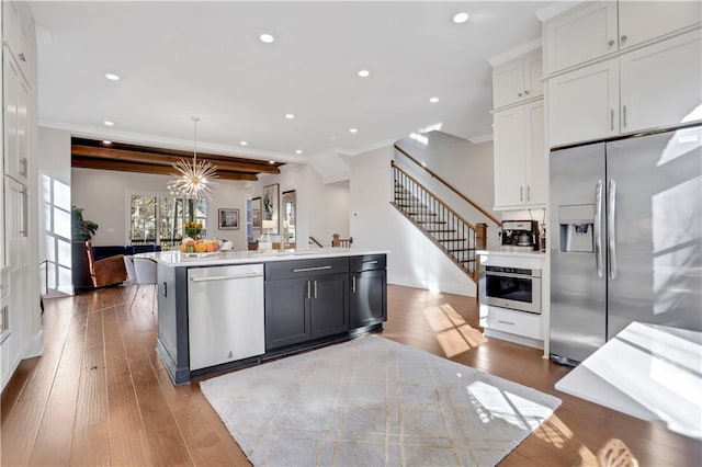 kitchen featuring decorative light fixtures, white cabinetry, appliances with stainless steel finishes, and a kitchen island with sink