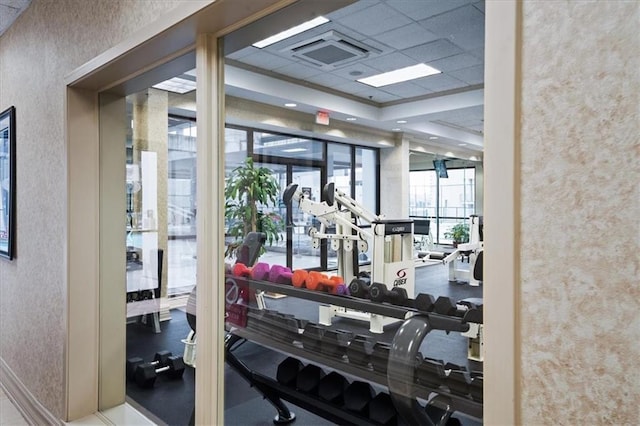 workout area featuring a paneled ceiling, a wall of windows, and a tray ceiling