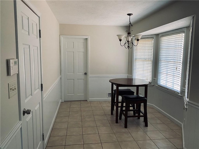 dining space featuring light tile patterned floors, a textured ceiling, an inviting chandelier, and wainscoting