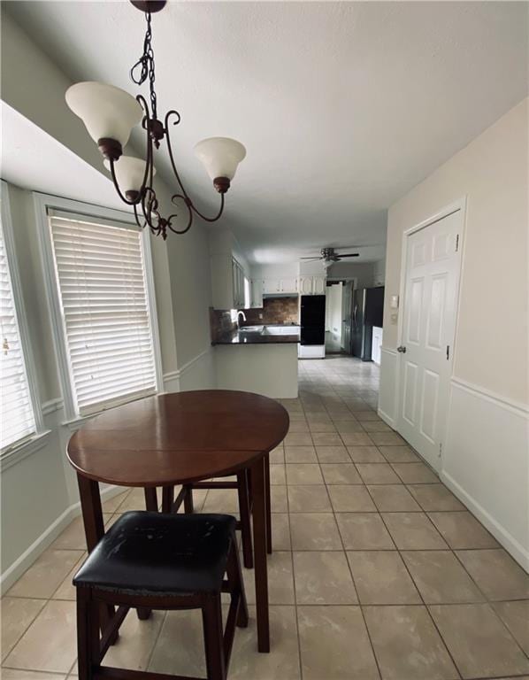 dining room with light tile patterned floors, baseboards, and ceiling fan with notable chandelier