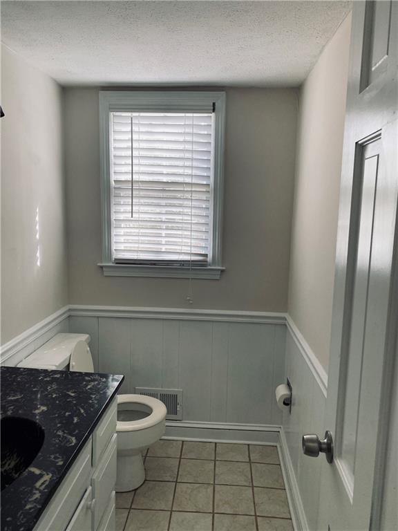 half bath featuring visible vents, a wainscoted wall, toilet, tile patterned floors, and a textured ceiling