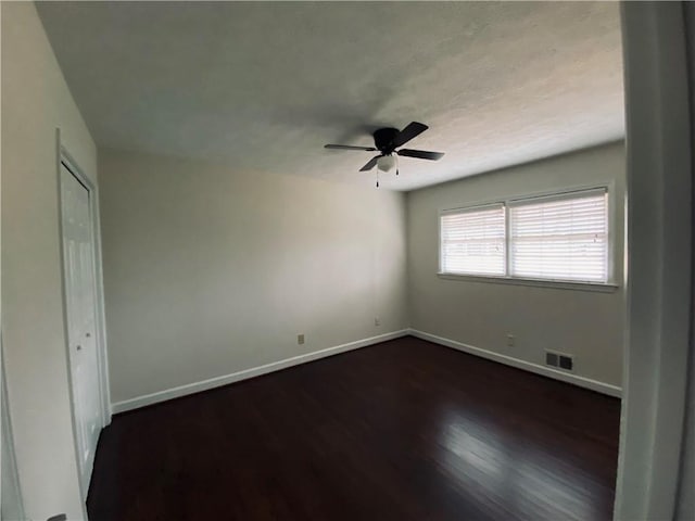 unfurnished room with visible vents, ceiling fan, dark wood-type flooring, and baseboards