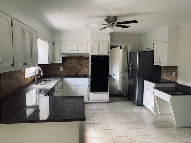 kitchen featuring dark stone countertops, light tile patterned floors, a sink, under cabinet range hood, and backsplash